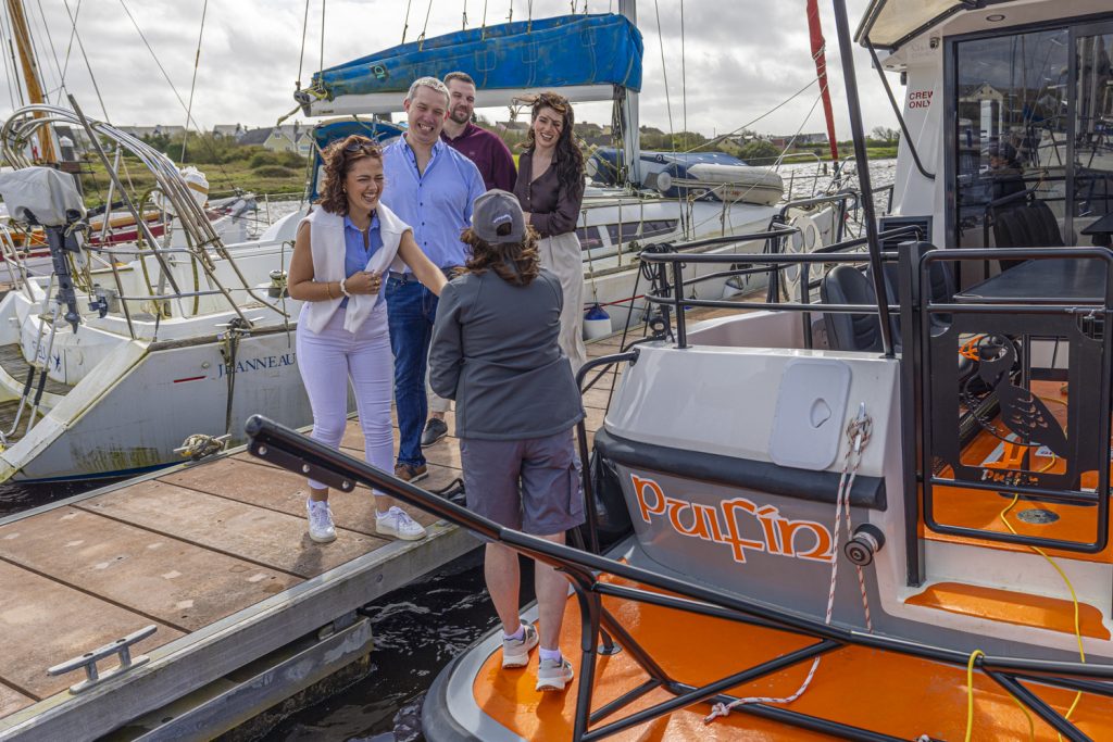 A group of guests stepping aboard Puifín from the pontoon, her name painted on the bow
