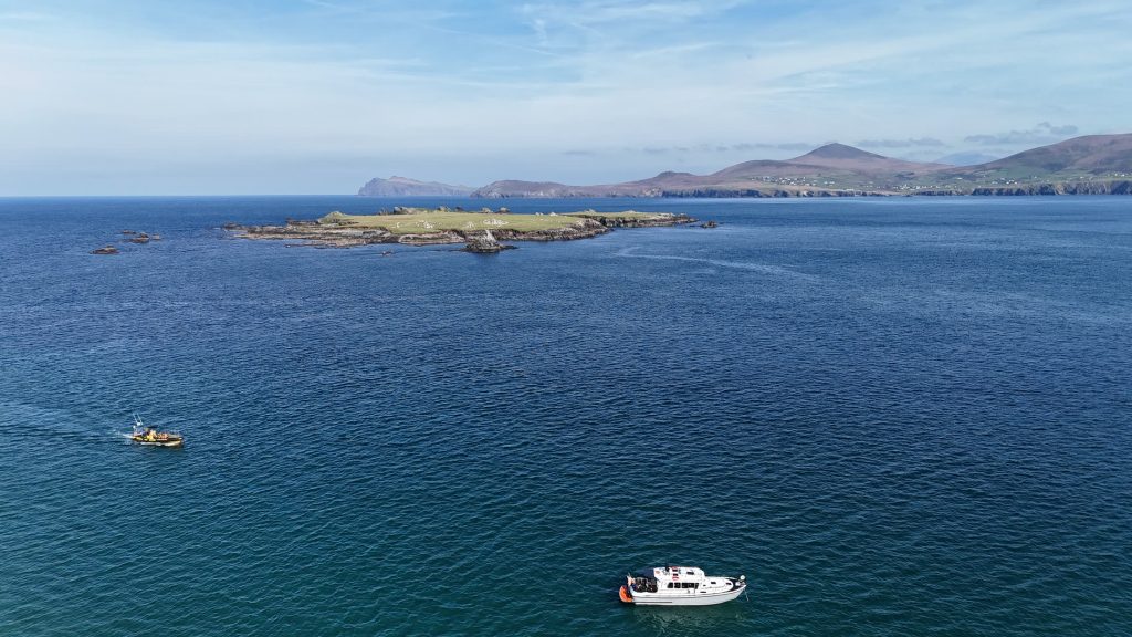 Wide aerial view of the Blasket Islands with Puifín and a second boat on deep blue water and the Kerry mountains beyond