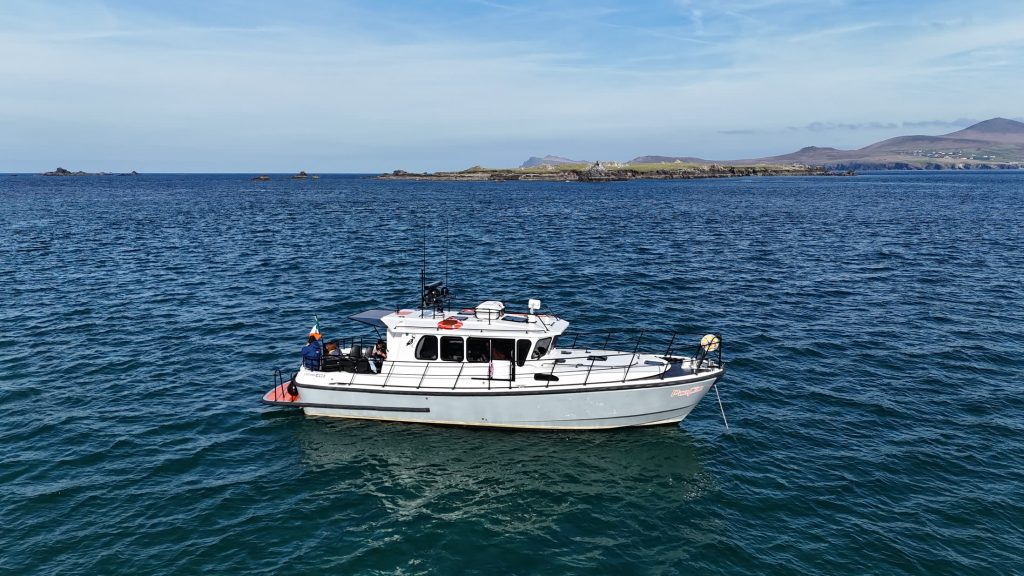 Side view of the charter boat Puifín on calm blue water, her name visible on the hull, with the Kerry coast behind